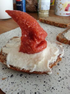 Kleiner frecher Mettesser mit Alienmaske auf Getreidemitmetttzipfelbukostullen